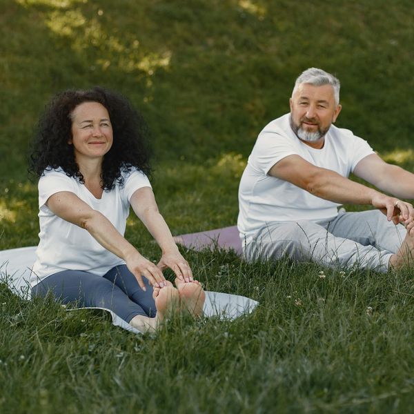 Smiling senior man doing a gentle arm exercise in a green park.